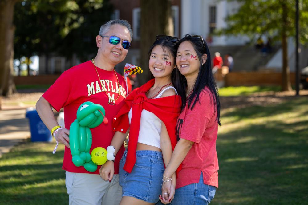 3 people standing close in red and white shirts, holding a kermit ballon animal