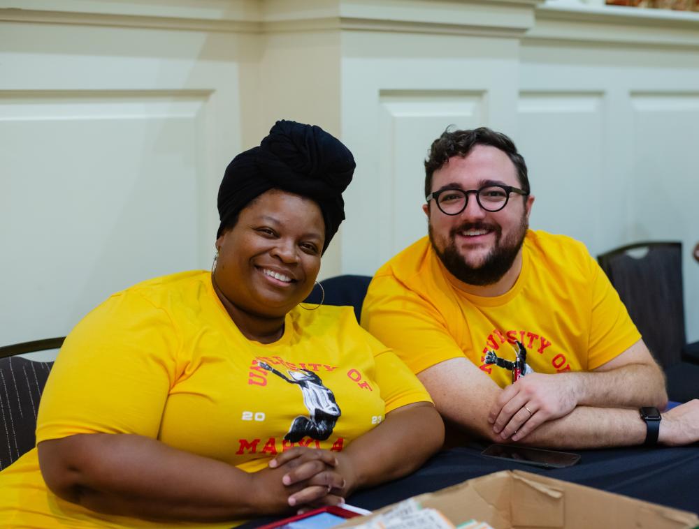 two people wearing yellow shirts sitting at a table, smiling